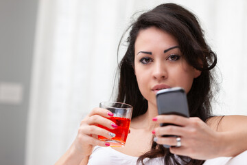 Fototapeta premium Young woman enjoying a cocktail while using her mobile phone