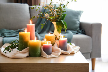 Fototapeta na wymiar Burning candles and plant branches on wooden table in room