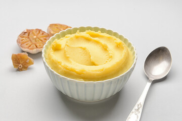 Bowl of tasty mashed potatoes with garlic on light background