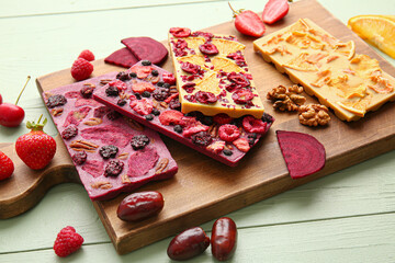 Handmade chocolate bars with fruits, berries and nuts on color wooden background, closeup