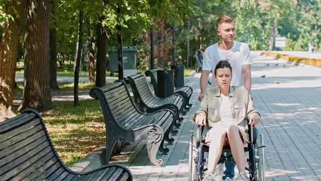 A couple walking in park - a guy rides a woman in a wheelchair