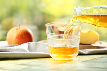 Pouring tasty apple juice from bottle into glass on table outdoors, closeup