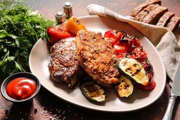 Plate with tasty pork steaks, tomato sauce and grilled vegetables on grunge background