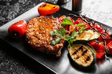 Plate with tasty pork steak and grilled vegetables on dark background, closeup