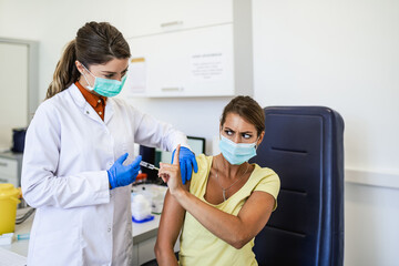 Female doctor or nurse trying to give shot or vaccine against virus to a scared patient. Angry and distrustful patient refuses to receive it.