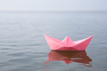 Pink paper boat on water surface, space for text