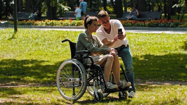 Woman in a wheelchair and her friend spending time at the summer park and taking a selfie together