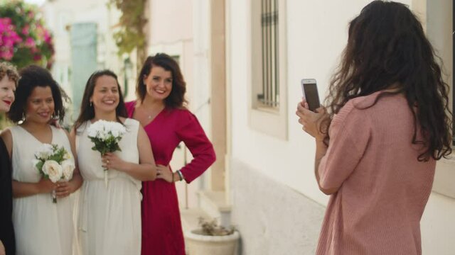 Girl taking picture of lesbian couple with friends at wedding. Slider shot of happy women in beautiful dresses, smiling, mugging and posing for camera. Friendship, LGBT wedding, photoshoot concept