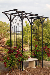 Springtime Flower garden with black metal trellis and concrete bench surrounded by red flowers and...