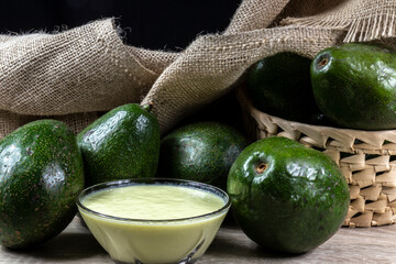 avocados fruits and avocado cream in glass bowl on the wooden table, with jute and black background in Brazil