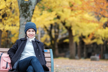 Happy woman enjoy at the park outdoor in Autumn season, Asian traveler in coat and hat against Yellow Ginkgo Leaves background