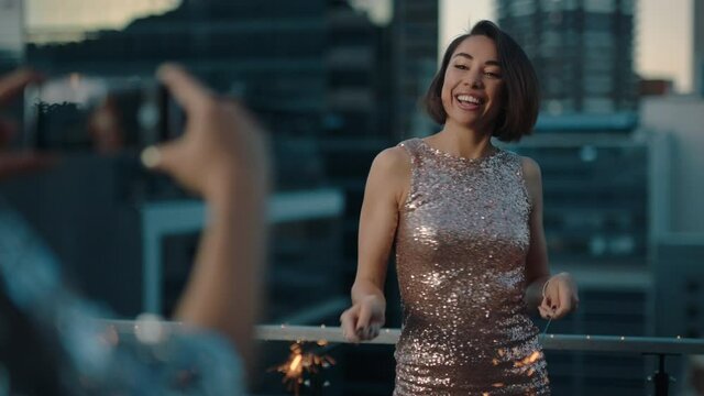 beautiful young woman dancing with sparklers celebrating new years eve at glamorous party wearing stylish fashion with friend using smartphone sharing video of celebration on social media