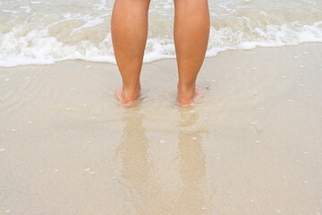 Asian female legs standing on wet sand beach