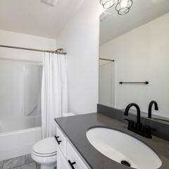 Square frame Bathroom interior with black fixtures and one piece shower tub with white shower curtain