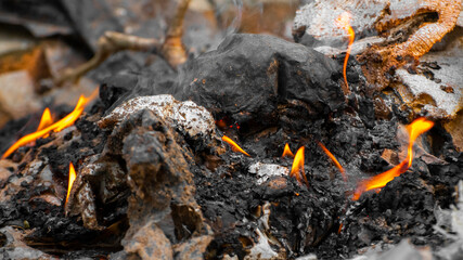 Burning the trash collection outside. Burnt ashes and the sparks of small flames close up.