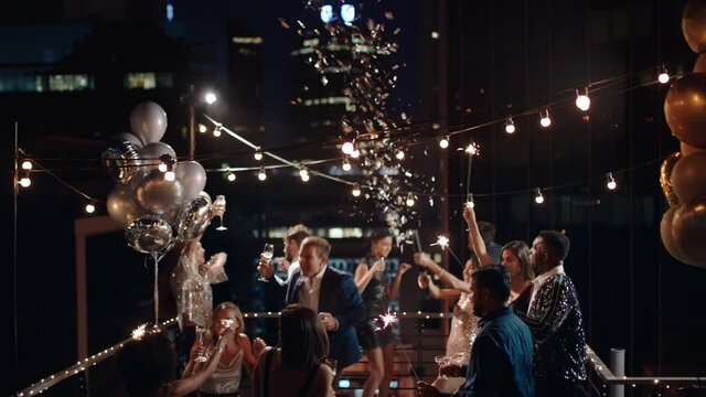 friends celebrating new years eve party dancing throwing confetti enjoying glamorous celebration wearing stylish fashion at formal social gathering on rooftop at night 4k 