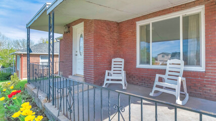 Pano Rocking chairs on the front porch of a house with red brick wall and white door