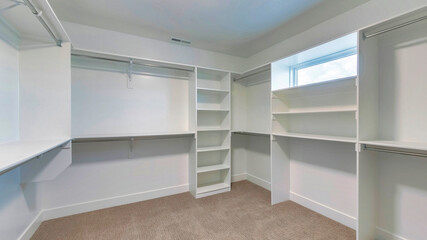 Pano Walk in closet of house with empty built in shelves and two levels clothing rods