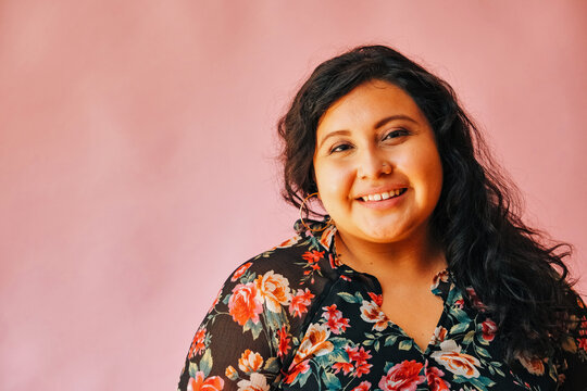 Portrait of smiling young woman wearing floral top against pink wall at home