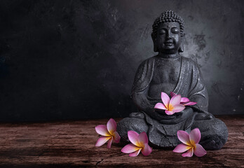 Buddha statue with frangipani flowers on a dark background - 454870129