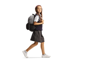 Full length shot of a schoolgirl in a uniform carrying a backpack and walking while looking at camera - obrazy, fototapety, plakaty