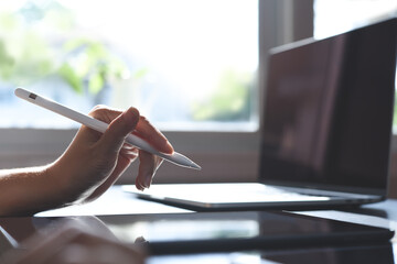 Woman using stylus pen on digital tablet and working on laptop computer from home office, close up