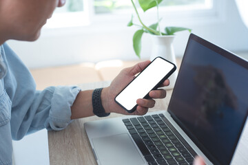 Mockup image of mobile phone, business man hand holding blank screen mobile phone during working on laptop computer at home office