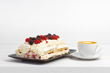 Homemade delicious meringue dessert with berries and cup of coffee cappuccino on white wooden table. Copyspace.