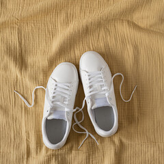White female sneakers on yellow crumpled muslin cloth background. Flat lay, top view. Merchandise, marketing, sale, shopping concept