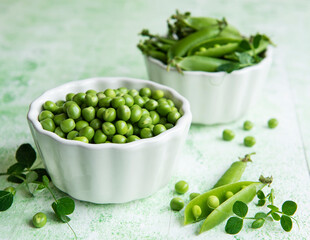 Fresh green peas pods and green peas with sprouts on green wooden background.