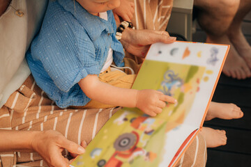Cute little girl pointing at pictures in book. Toddler sitting on her mother laps and reading book....