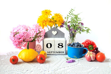 Calendar for September 8 : the name of the month in English, cubes with the numbers 0 and 8, ripe vegetables, bouquets of various flowers, blueberries in a blue cup on a gray napkin, white background