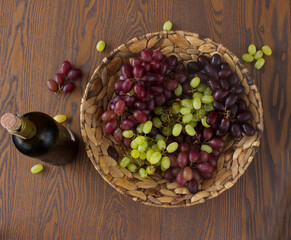a fruit basket with full of green and red grapes, a wine bottle, a goblet on a woodden table 5