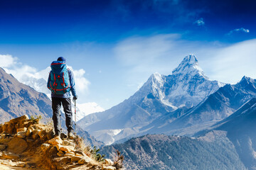Wandelaar met trekkingstokken staat op de helling tegen de achtergrond van hoge besneeuwde bergen