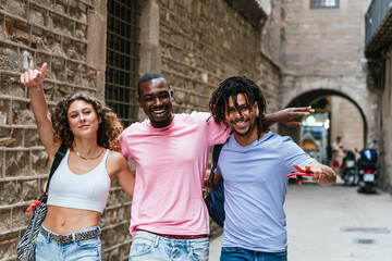 multi-ethnic group of friends walking embraced through the streets of Barcelona. They dress summer attire and smile looking at camera