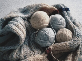 Knitting a scarf or sweater from gray, beige yarns. Balls of woolen and acrylic threads. Knitting as a hobby. Accessories, knitting needles, crochet hooks.