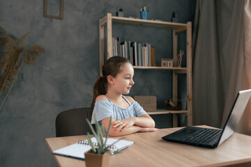 Teenage schoolgirl doing homework with laptop at home. The child uses gadgets for study.