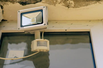 Motion sensor and LED spotlight on the wall of the building. Automatic building perimeter lighting system. Protection of private property.