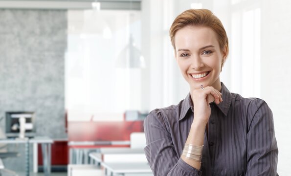 Confident young white businesswoman smiling in modern business office. Portrait of adult woman in 20s, happy confident smile. Copy space.