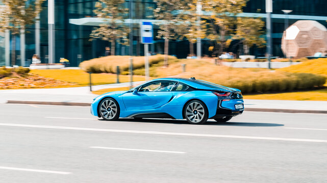 BMW i8 plug-in hybrid is driving along the street with an autumn urban background