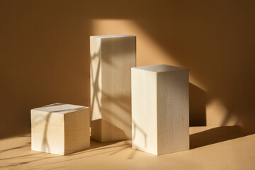 Geometric 3d podiums made of wooden material, arranged in steps on beige background in rays of sunlight. Shadows from branches fall on objects. Concept of presentation of cosmetic products