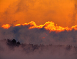 Dramatic scene including fiery sunrise on extremely cold winter morning with sea fog and clouds appearing as if in flame or as ablaze and sun barely visible trough clouds / sea smoke.