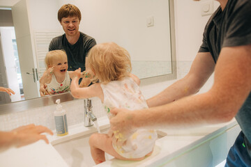 Funny little girl and father grimacing at mirror in bathroom. Man having fun with his child at...