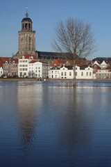 Fototapeta na wymiar The facades of beautiful old buildings and the tower of the Great Church in the city of Deventer, The Netherlands, with reflection in the river IJssel