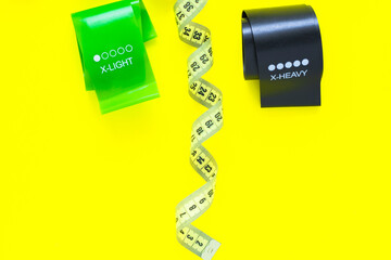 Two fitness tapes of black and green color are located at the top of the photo on a yellow...