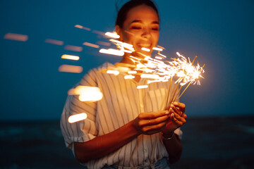 Glowing sparkles in hands. Women with Christmas sparklers on nature and twillight sky background....