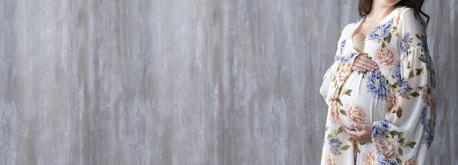 Pregnant girl in dress on grey wall background. Copy Space.