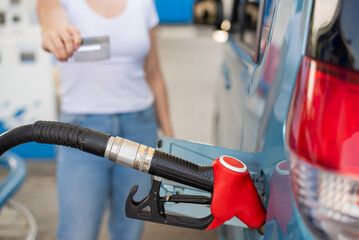 Fototapeta premium A woman fills her car with gasoline at a self-service gas station and holds a credit card
