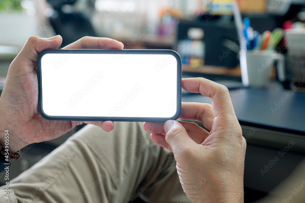 Wall mural Cropped shot of man hand holding blank white screen smartphone in horizontal view while sitting at office.