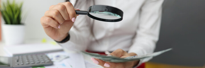 Female hand holds magnifying glass and cash at work table
